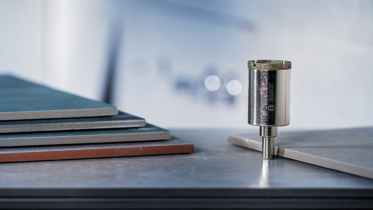 Deimantinis gręžimo karūnos antgalis, stovintis vertikaliai šalia sukrautų keraminių plytelių.