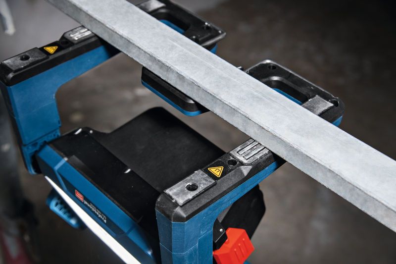 Belaidis darbo vietos žibintas apšviečia darbo vietą po metaline sija.