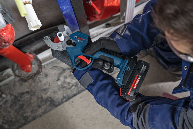 Asmuo, dėvintis apsaugos priemones, pjauna plastikinį vamzdį akumuliatorinėmis vamzdžių žirklėmis.