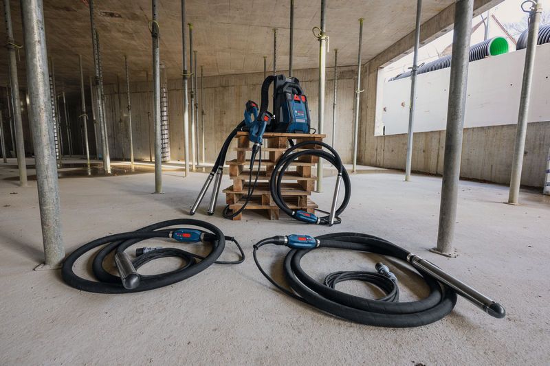 Statybvietė su dviem betono vibratoriais ir kuprinės formos maitinimo šaltiniu ant padėklo.