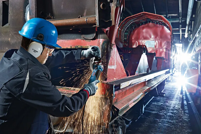 Persona drošības aprīkojumā slīpē metālu uz liela industriāla dzelzceļa vagona.