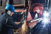 Persona drošības aprīkojumā slīpē metālu uz liela industriāla dzelzceļa vagona.