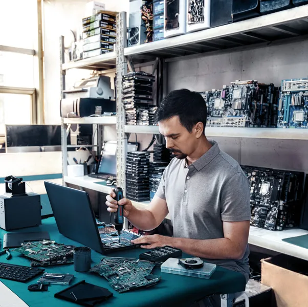 Cilvēks izmanto akumulatora skrūvgriezi, lai saliktu elektroniskas detaļas pie darbagalda.