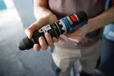 Cilvēks telpās tur FlexiClick adapteri elektroinstrumentam.