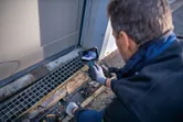 Persona, kas valkā drošības aprīkojumu, pārbauda drenāžas režģi, izmantojot pārbaudes kameru.