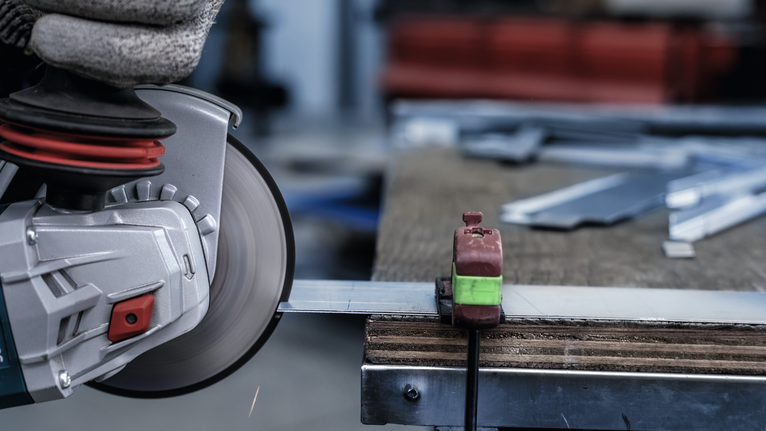 Persona, kas valkā drošības aprīkojumu, griež metālu ar ripzāģi.