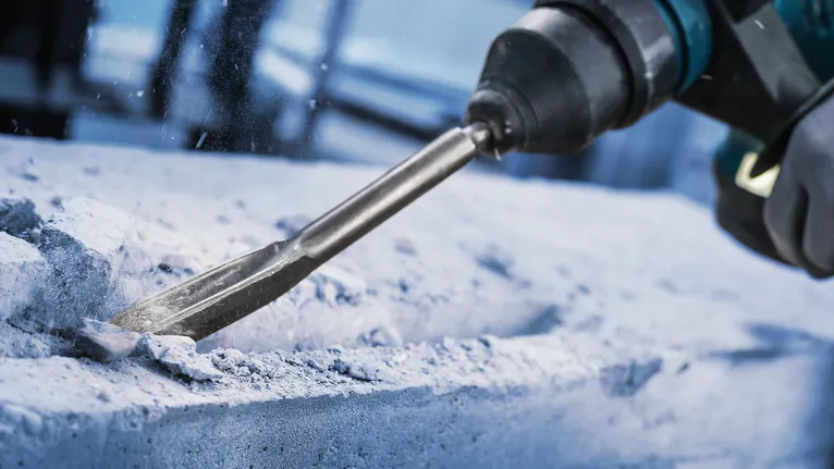 Persona, kas valkā drošības aprīkojumu, izmanto rotācijas āmuru, lai kaltu betonu.