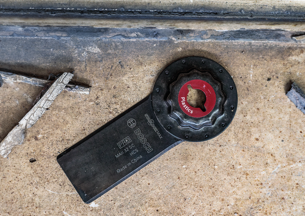 Oscilējošs instrumenta asmens plastmasas griešanai, kas atrodas uz betona virsmas.