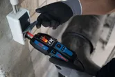 Persona, kas valkā drošības aprīkojumu, izmanto sprieguma testeri elektroinstalācijai.