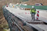 Persona, kas valkā drošības aprīkojumu, darbina āmuru šosejas būvlaukumā.