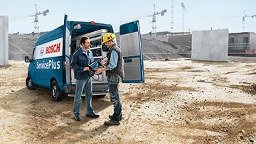 Divi vīrieši sarunājas blakus Bosch ServicePlus furgonam būvlaukumā.