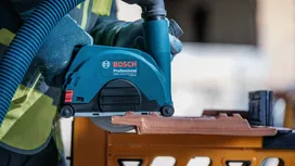 شخص يرتدي معدات السلامة يقطع بلاطة سيراميك باستخدام أداة كهربائية.