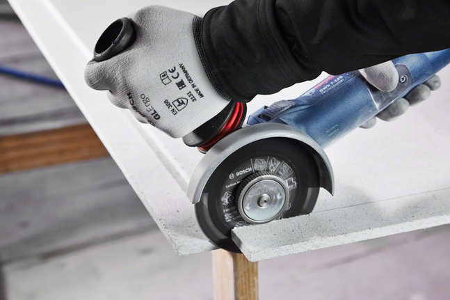 Person wearing safety equipment cuts a fiber cement board with a handheld angle grinder.