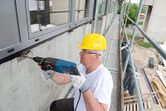 A person wearing safety equipment drills into concrete at a construction site.