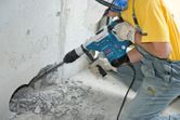 A person wearing safety equipment drills into concrete with a rotary hammer.