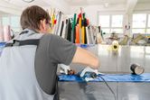 A person wearing safety equipment uses a heat gun to seal plastic sheets on a worktable.