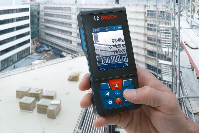 A person holds a laser measure displaying distance readings on a construction site.
