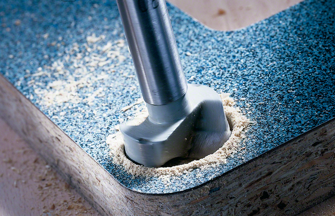 Forstner bit drilling a clean circular hole in a laminated wood board.
