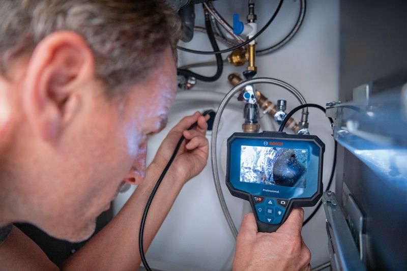 Person inspects pipes with an inspection camera in a confined space.