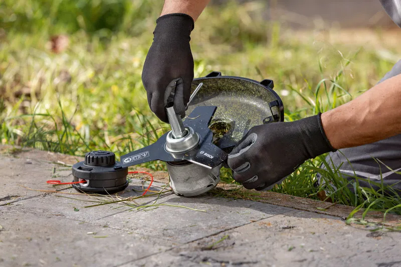 A person wearing safety equipment adjusts the head of a cordless brushcutter on grass.