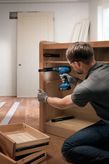 Person wearing safety equipment installs cabinet drawer slides using a cordless drill.