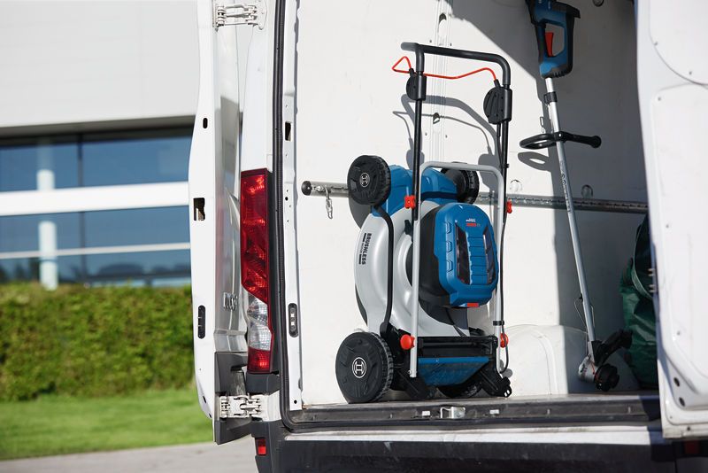 Folded cordless lawn mower and trimmer stored in the back of a white work van.