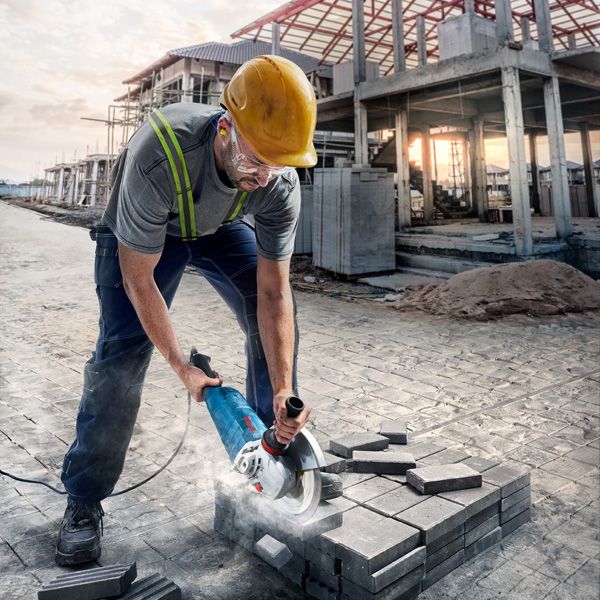 A person wearing safety equipment cuts pavement blocks using a power cutter at a construction site.