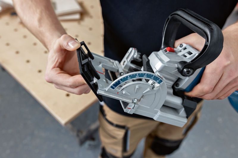 A person wearing safety equipment adjusts a biscuit joiner in a workshop.