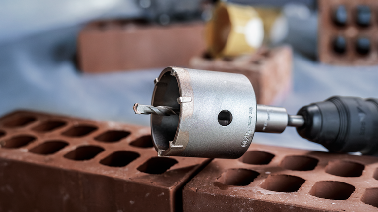 A core drill bit attached to a power tool positioned above hollow bricks.