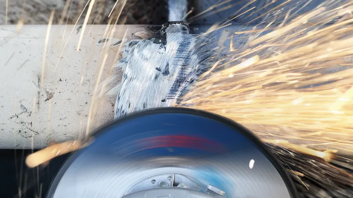 Angle grinder cutting metal pipe, creating sparks.