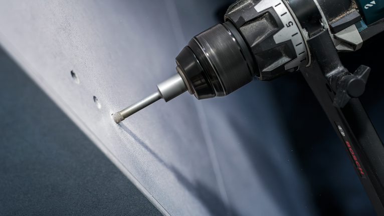 Power tool drilling clean holes into a white wall panel.