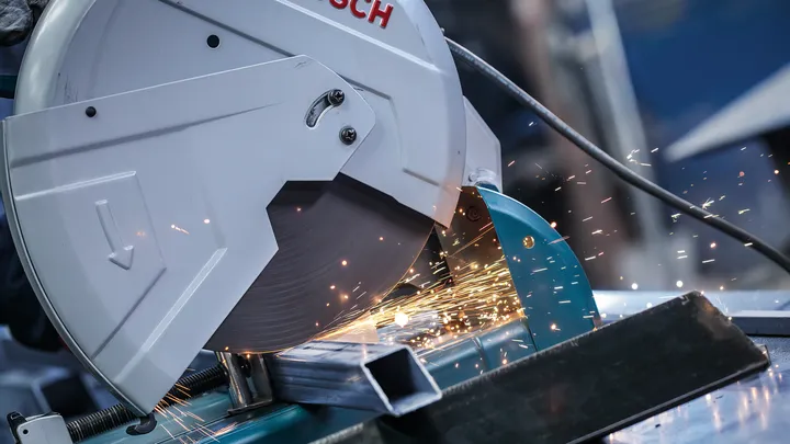 Metal cutting saw producing sparks while cutting a steel tube.