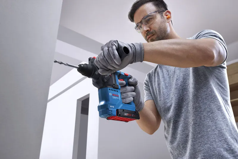 Person wearing safety equipment drills into a wall with a rotary hammer.