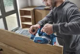 A person wearing safety equipment smooths a wooden board using an electric planer.