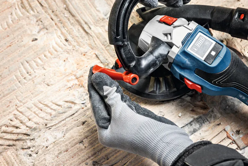 A person wearing safety equipment adjusts a concrete grinder on a textured floor.