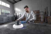 A person wearing safety equipment uses a polisher on a large metal surface.