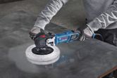 A person wearing safety equipment polishes a metal sheet using a power polisher.