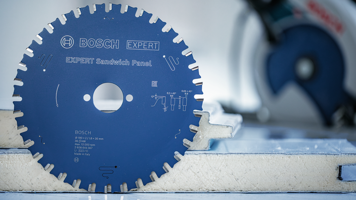 Circular saw blade displayed upright on a foam panel, a saw is blurred in the background.