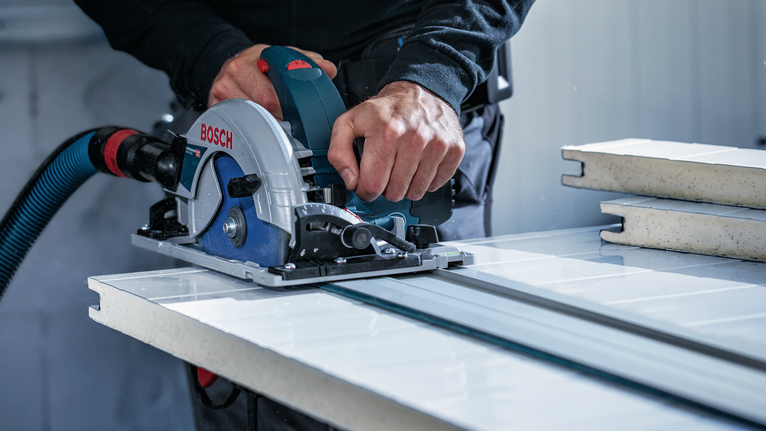 Person operates a circular saw along a guide rail cutting large tile panels.