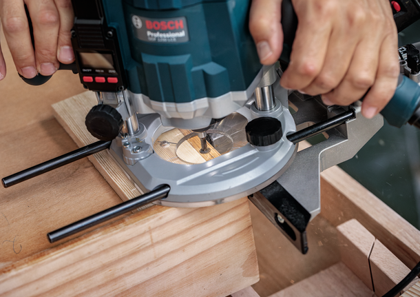 Person guides a power router cutting a groove in a wooden board.