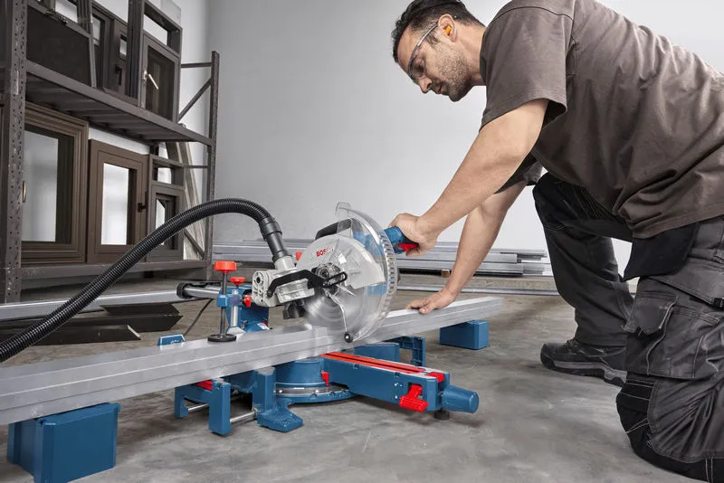A person wearing safety equipment cuts a metal beam using a mitre saw.