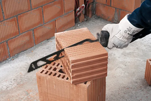 Une personne portant un équipement de sécurité coupe une brique creuse avec une scie électrique.