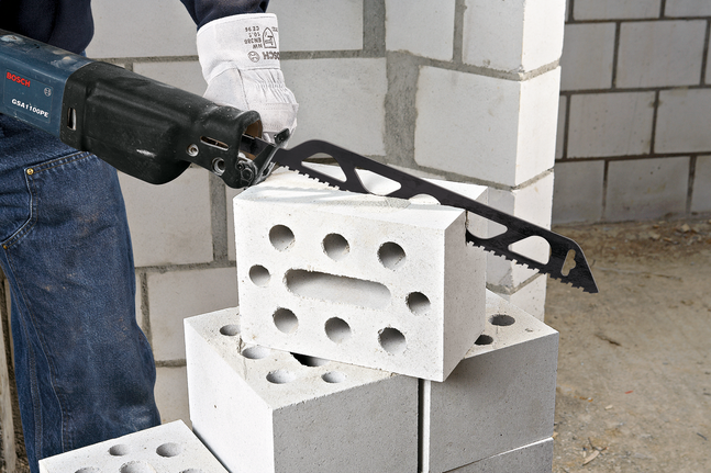 Une personne portant un équipement de sécurité coupe un bloc de béton avec une scie alternative.
