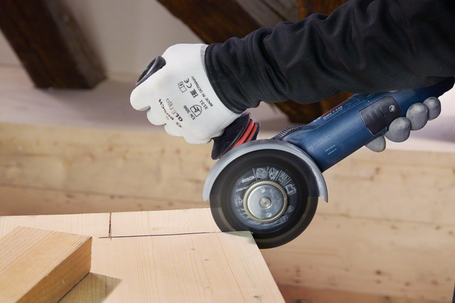 Une personne portant un équipement de sécurité utilise une meuleuse d'angle pour couper une planche de bois.