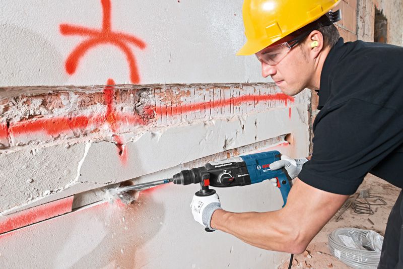 Une personne portant un équipement de sécurité utilise un marteau perforateur pour creuser une rainure dans un mur en béton.