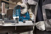 Une personne portant un équipement de sécurité découpe une tôle de métal à l'aide d'une scie sauteuse.