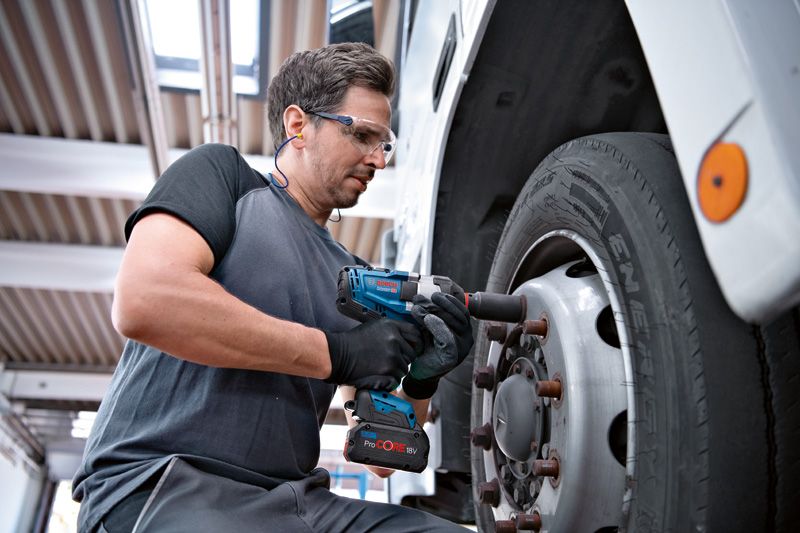 Une personne portant un équipement de sécurité utilise une clé à chocs sur une roue de camion.