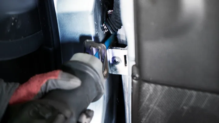 Une personne portant un équipement de sécurité utilise une scie alternative pour couper du métal à l’intérieur d’un véhicule.