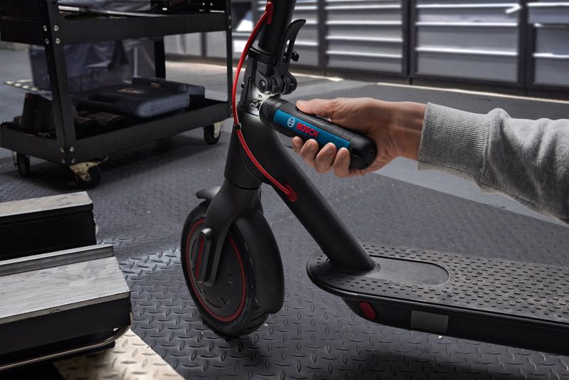 Une personne utilise un tournevis sans fil pour régler le guidon d’un scooter électrique.