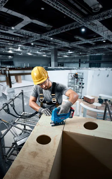 Une personne portant un équipement de sécurité utilise une scie sauteuse pour couper du bois sur un chantier de construction.
